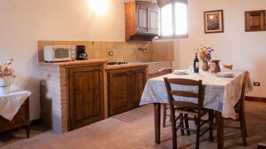 A rustic kitchen with wooden cabinets, a tiled backsplash, a microwave, and a dining table set for two. - Cosy apartment in villa for 3 guests with WIFI, TV, patio and pets allowed (Roccastrada)