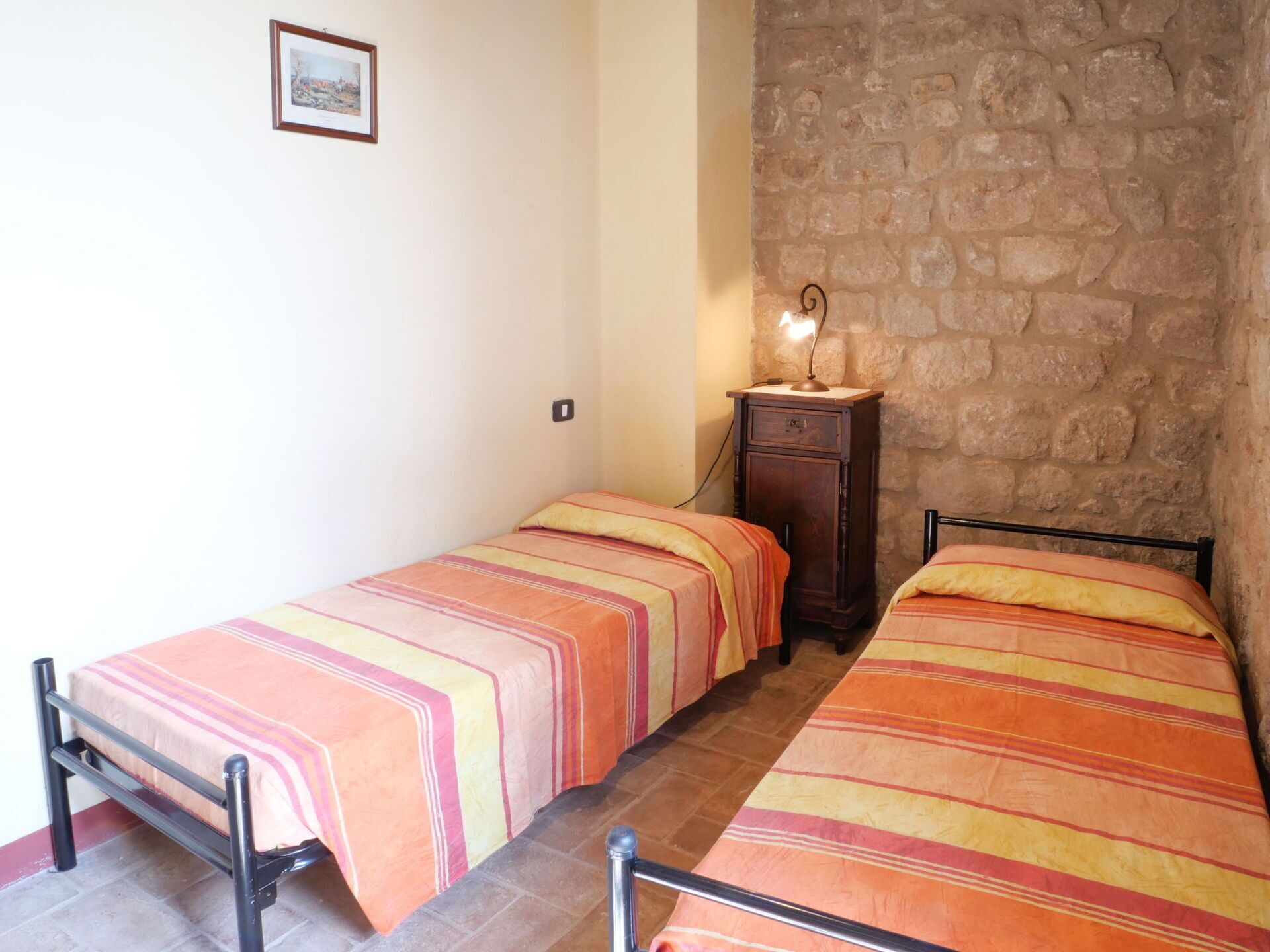 A small, cozy room with two single beds, a wooden cabinet, and a stone wall.