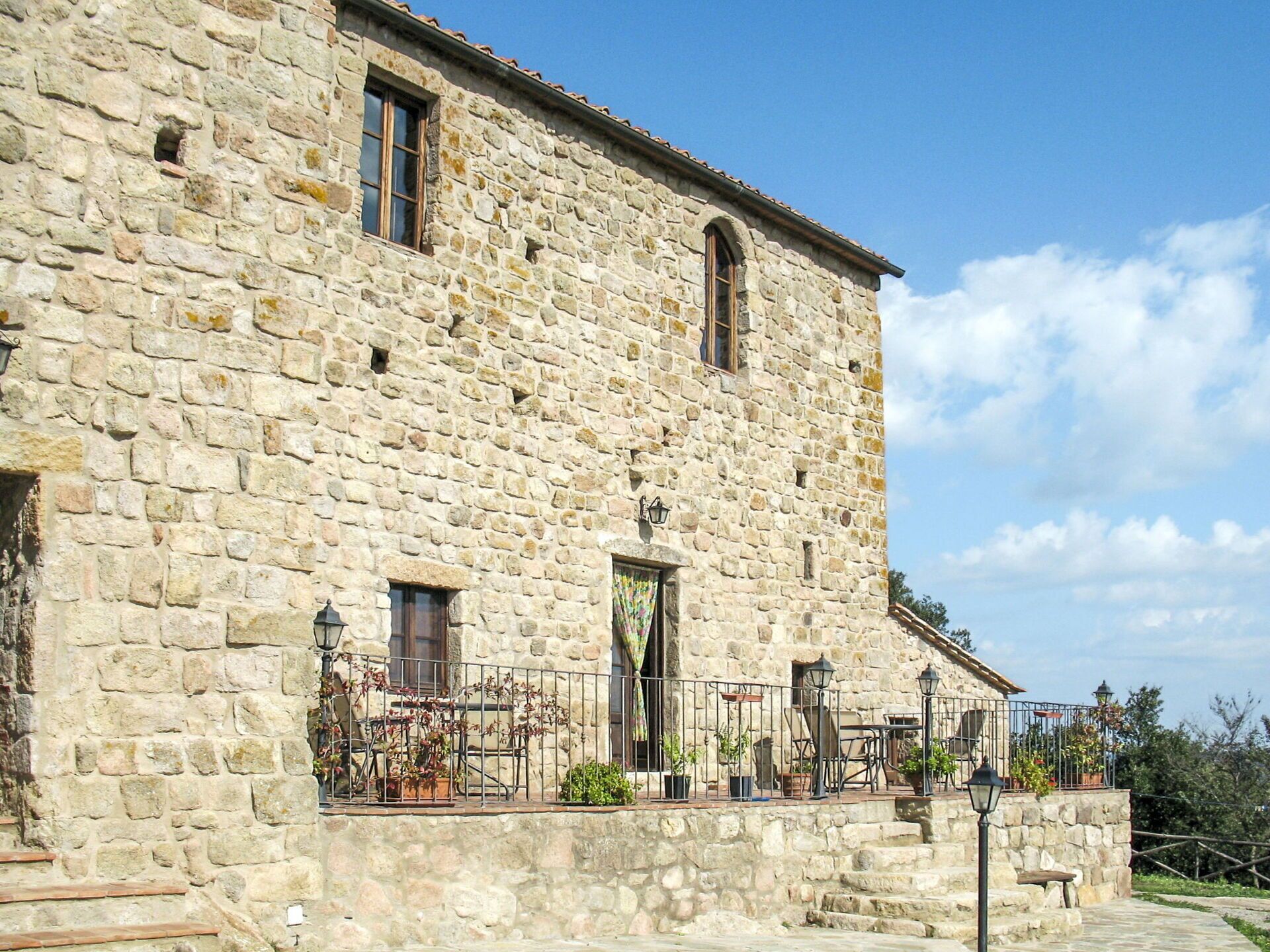 Un edificio de piedra con balcón, mobiliario exterior y una escalera que conduce a la entrada.