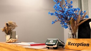 A reception desk with a payment terminal, a vase with blue flowers, and a wooden sign that reads 'Reception'.