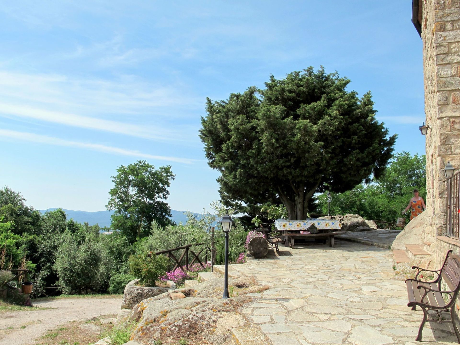 A stone pathway leading to a bench, a large tree, and a stone building with a balcony.