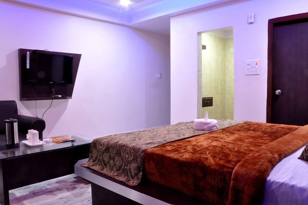 Ein Hotelzimmer mit Bett, Schreibtisch mit Computer, flachbildschirmfernseher an der Wand und einem durch eine Glastür sichtbaren Badezimmer.
