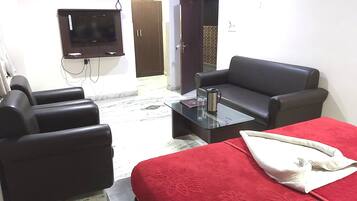 A hotel room with a bed, a sofa, a coffee table, a TV, and an air conditioning unit.