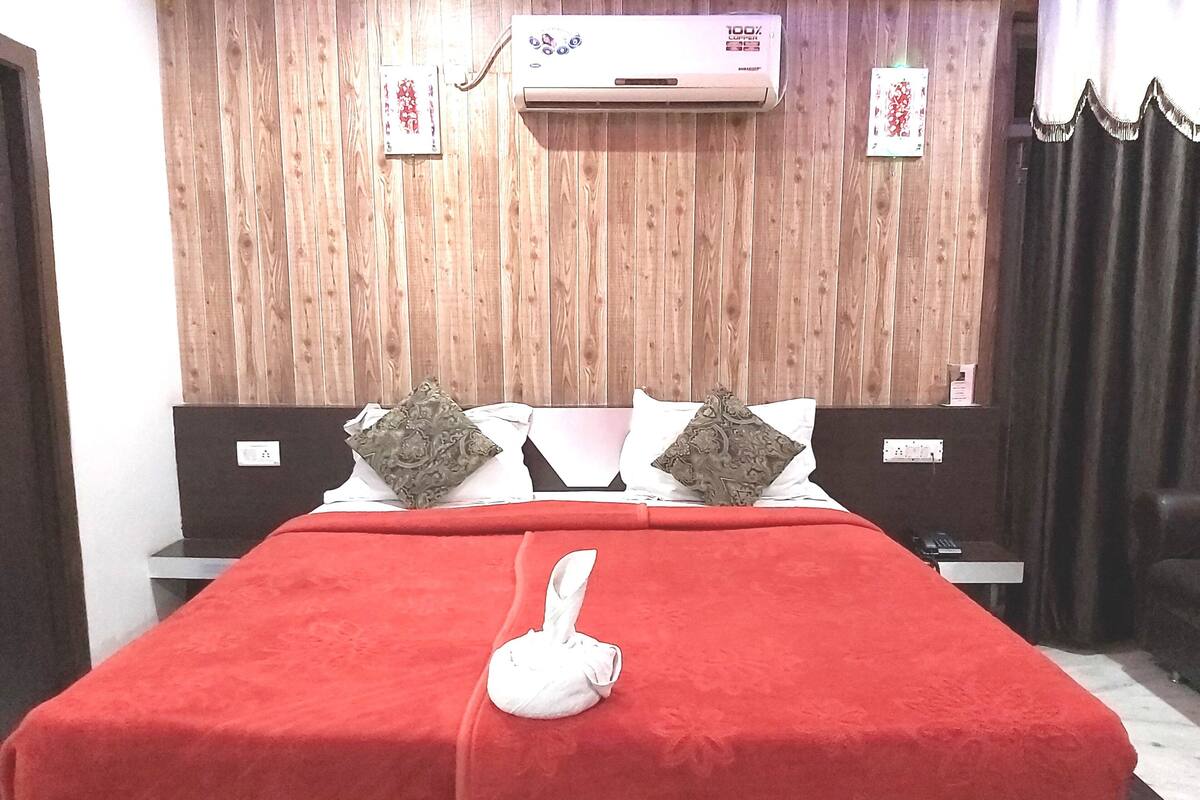 Ein Hotelzimmer mit einer Wandpaneele aus Holz, einem Bett mit roter Bettdecke, zwei Zierkissen, einem weißen Handtuch und einer Klimaanlage.