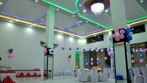 A spacious hall with white chairs, a table with a red and white tablecloth, and decorative balloons. - Neelam Palace Hotel (Singrauli)