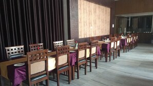 A dining area with wooden tables and chairs, a large wooden panel wall, and a tiled floor. - Neelam Palace Hotel (Singrauli)