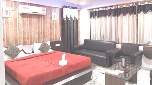 A hotel room with a bed, a sofa, a glass coffee table, and a ceiling fan. - Neelam Palace Hotel (Singrauli)
