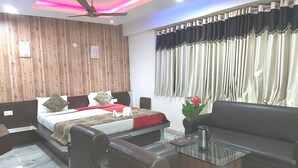 A modern bedroom with a wooden headboard, a bed with decorative pillows, a glass coffee table, and a leather sofa. - Neelam Palace Hotel (Singrauli)