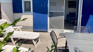 Ein Hotel Eingang mit der Nummer 177, einer Schiebetür, Außenbereich mit Stühlen und einem Tisch sowie ein sichtbarer Innenbereich mit einem Bett und einer Couch.