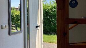 Ein zur Außenwelt führender Durchgang mit einer weißen Tür, einem kleinen Spiegel an der Wand und einem WLAN-Symbol.