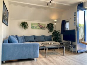 Un salon avec un canapé, une table basse, un téléviseur et des plantes.