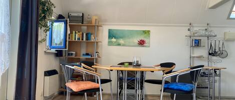 Un comedor con una mesa de madera, cuatro sillas, una estantería, un reloj y un cuadro.