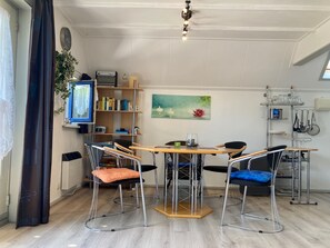 Un coin repas comprenant une table en bois, quatre chaises, une bibliothèque, une horloge et un tableau.