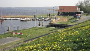 A marina with boats docked, a small building with a red roof, and a grassy area with yellow flowers. - 6 Pers Holiday Home Leonie With a Large Garden Close to the Lauwersmeer (Anjum)