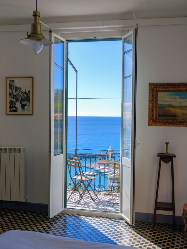 A room with a view of the sea, a bed, a radiator, and a painting on the wall.