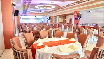 A banquet hall with round tables, brown chairs, and a red carpet.