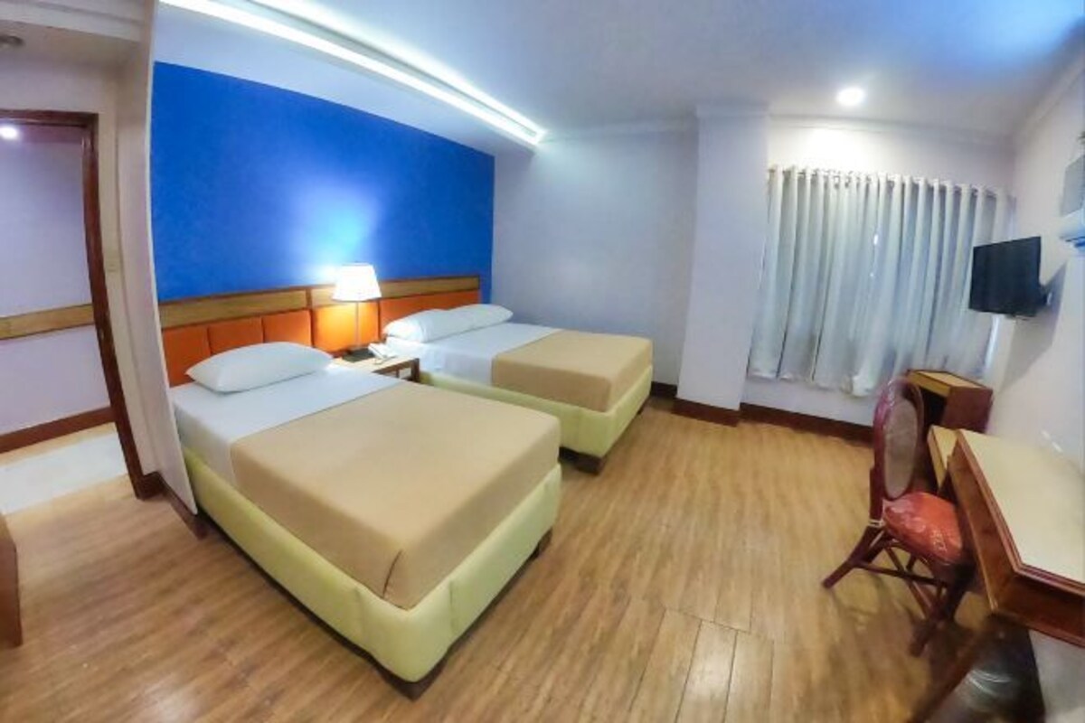 Habitación de hotel con dos camas, un escritorio, una silla, un televisor y una ventana con cortinas.