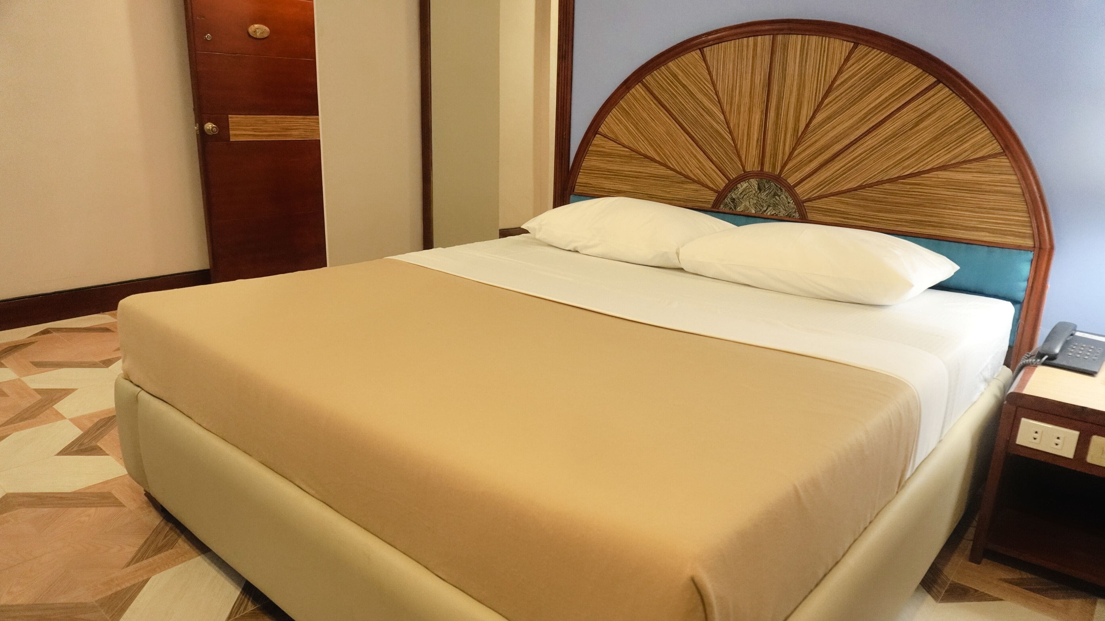 Habitación de hotel con cama, cabecero de madera, mesita de noche y una puerta.