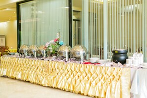 Una mesa de buffet con mantel dorado, vajilla para servir alimentos y una pieza decorativa central.