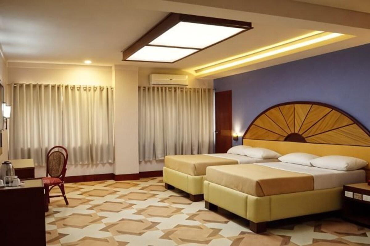 A hotel room with two beds, a desk, a chair, and a patterned floor.