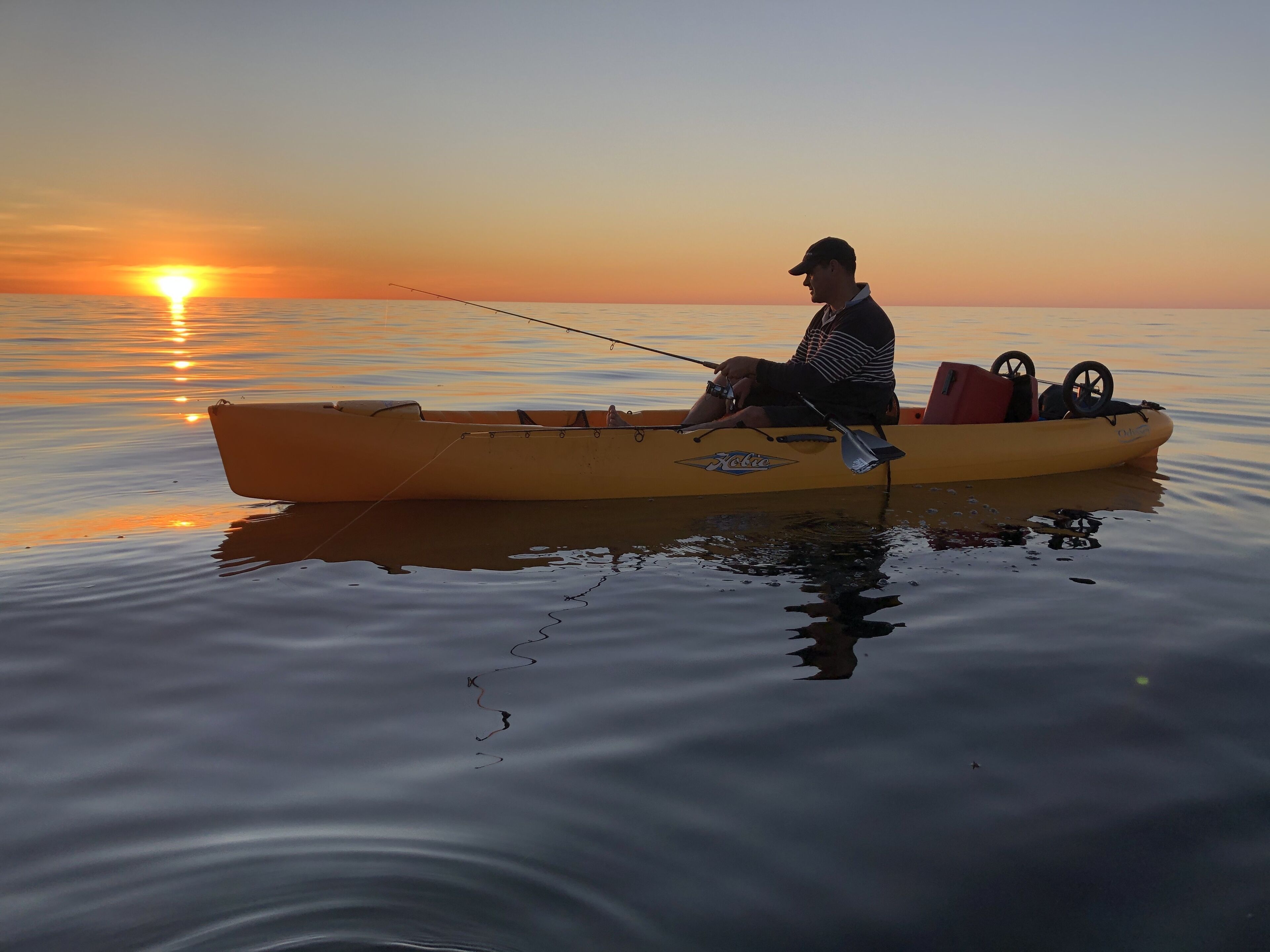 Een persoon in een gele kajak op kalm water tijdens de zonsondergang.
