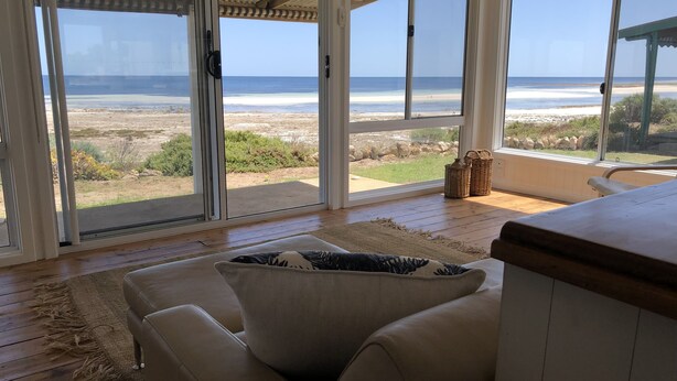Una habitación con un amplio ventanal corredizo que da a vistas de la playa, un sofá color beige y una alfombra tejida.