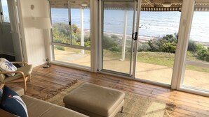 Una habitación con un sofá color crema, una lámpara de pie y vistas al océano a través de amplios ventanales correderos.