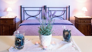 A neatly arranged bedroom with a bed, two bedside tables, a bedside lamp, a vase with flowers, and two candles on a table.
