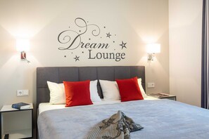 Ein Hotelzimmer mit einem Bett, zwei roten und weißen Kissen, einem grauen Kopfteil und einem Wandschild mit der Aufschrift 'Dream Lounge'.