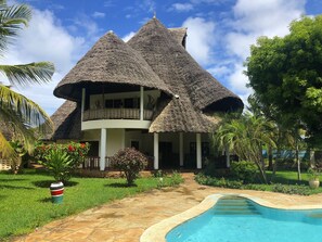 Une maison avec un toit de chaume et une piscine.
