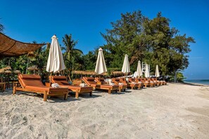 A beachside lounge area with wooden lounge chairs and white umbrellas, set against a backdrop of palm trees and a clear sky. - Ama-Lurra Villa (Gili Air)