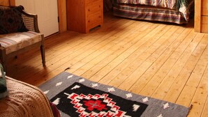 Een knus zolderkamer met een slaapkamer, een bed met een geruite plaid, een klein houten nachtkastje en een stoel.