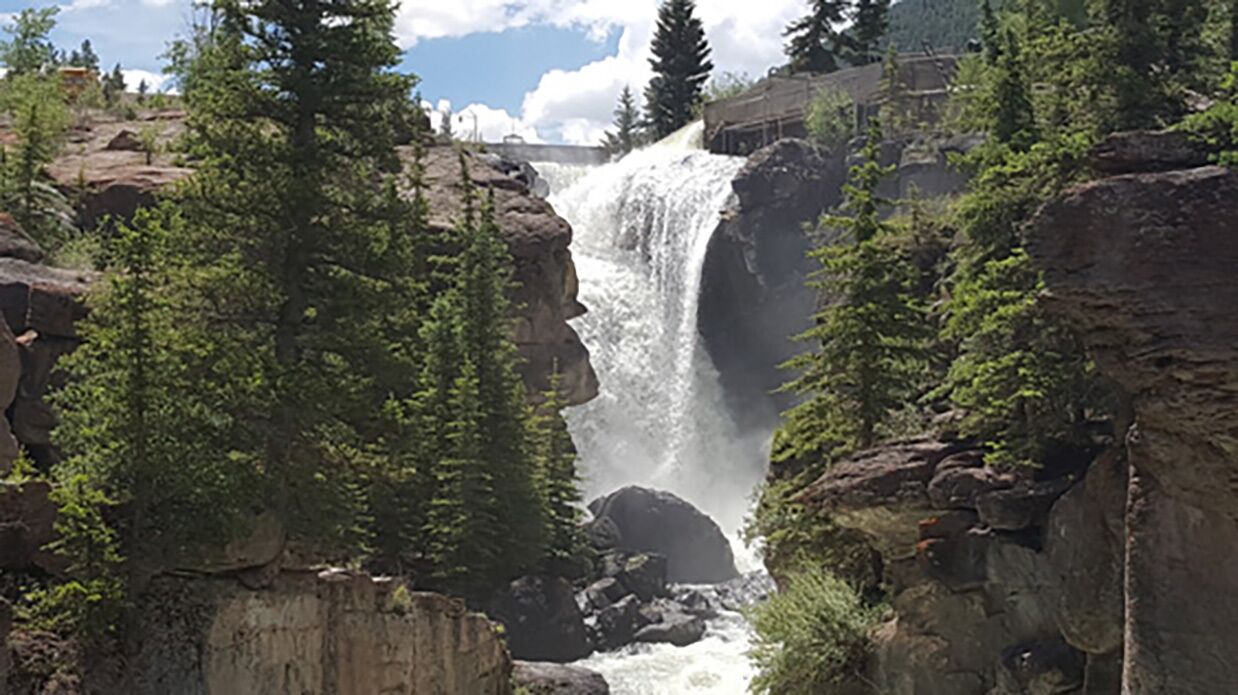 Una cascada rodeada de árboles verdes y terreno rocoso.