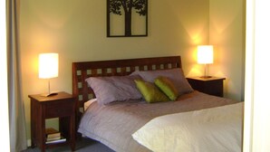 Un dormitorio con una cama, dos mesitas de noche con lámparas, un cabecero de madera y un cuadro colgado en la pared de un árbol.