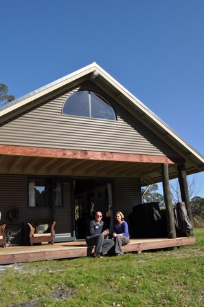 A house with a sloped roof and a large window. There is a porch with two people sitting. - Scotsdale Valley Studios (Scotsdale)