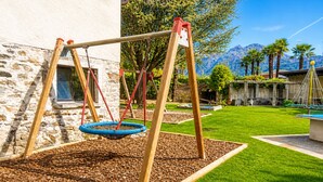 Un ensemble de balançoires dans un jardin, avec un mur en pierre, une piscine et une vue sur la montagne.