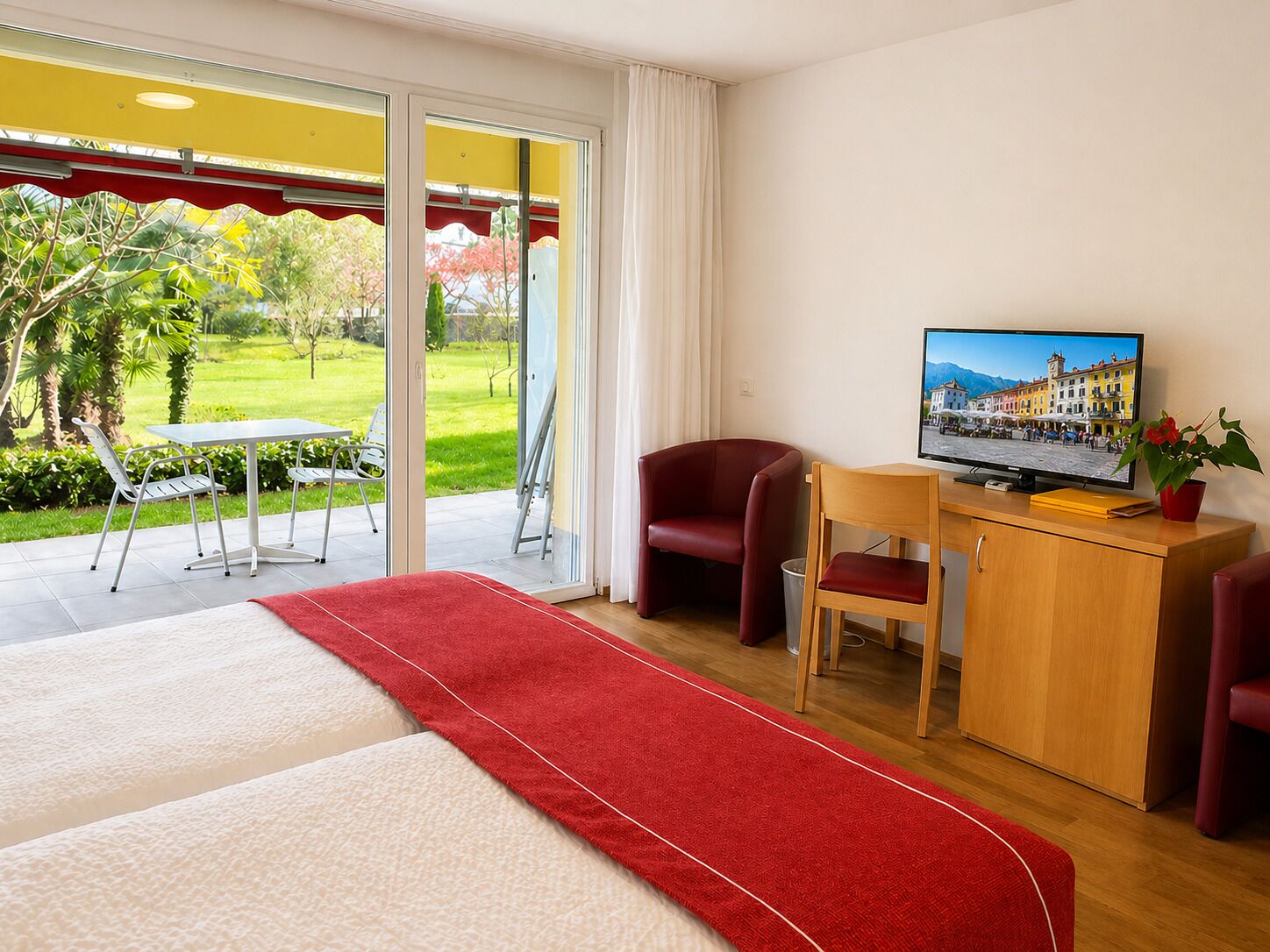Habitación de hotel con cama, escritorio con televisor, silla y vista a un jardín.