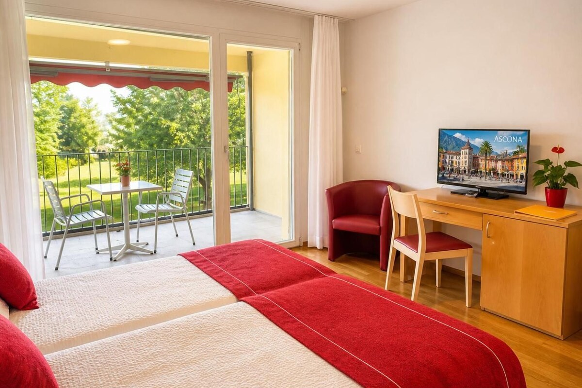 Habitación de hotel con balcón, televisor, escritorio y silla.