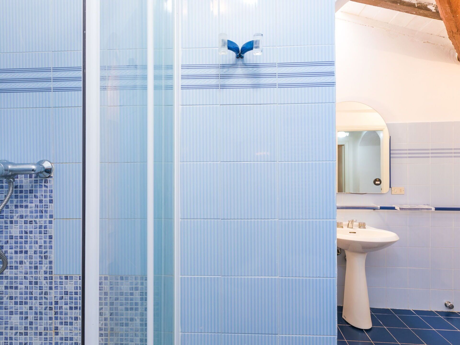 Een badkamer met een douche, wastafel en spiegel.