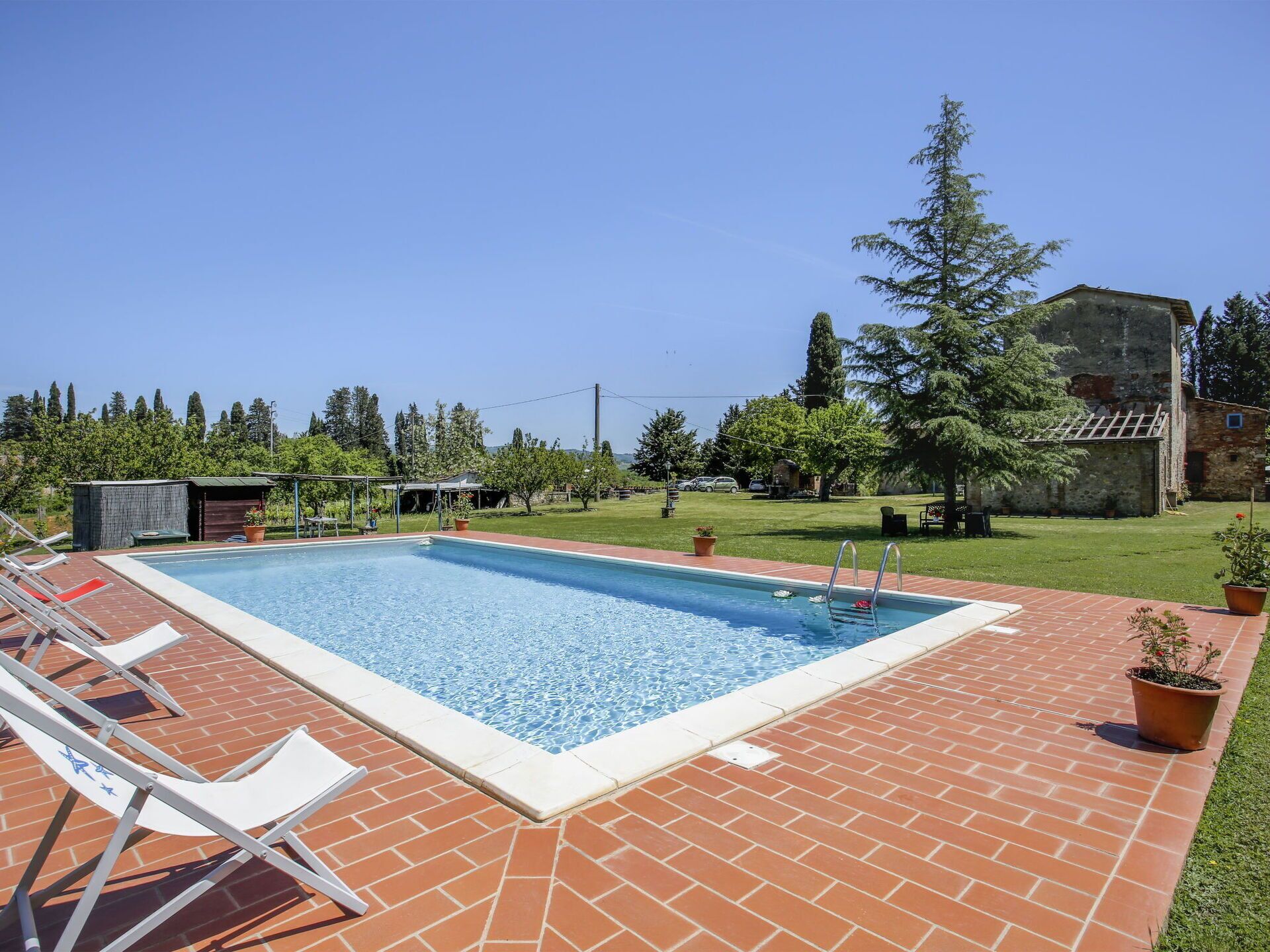 Une piscine rectangulaire, bordée d’une terrasse en briques, entourée d’une pelouse et d’arbres.