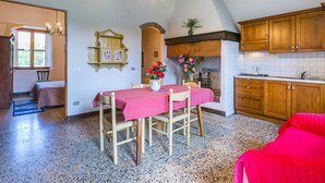 A cozy kitchen with wooden cabinets, a dining table with a red tablecloth, and a fireplace with flowers. - Nice apartment in villa for 5 guests with pool, WIFI, TV, patio, pets allowed and panoramic view (Monteriggioni)