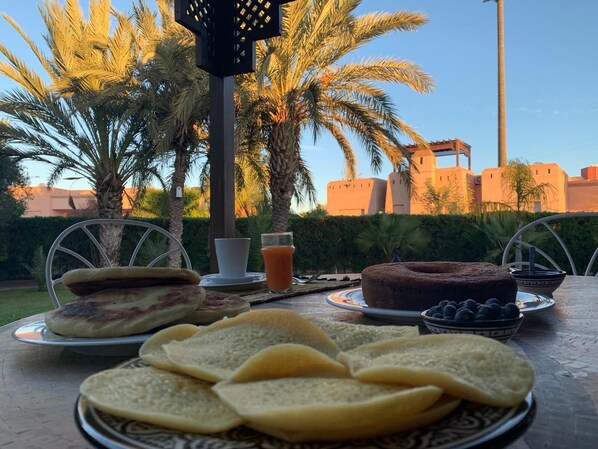 A table set outdoors with food items including sandwiches, a cake, and a bowl of blueberries.