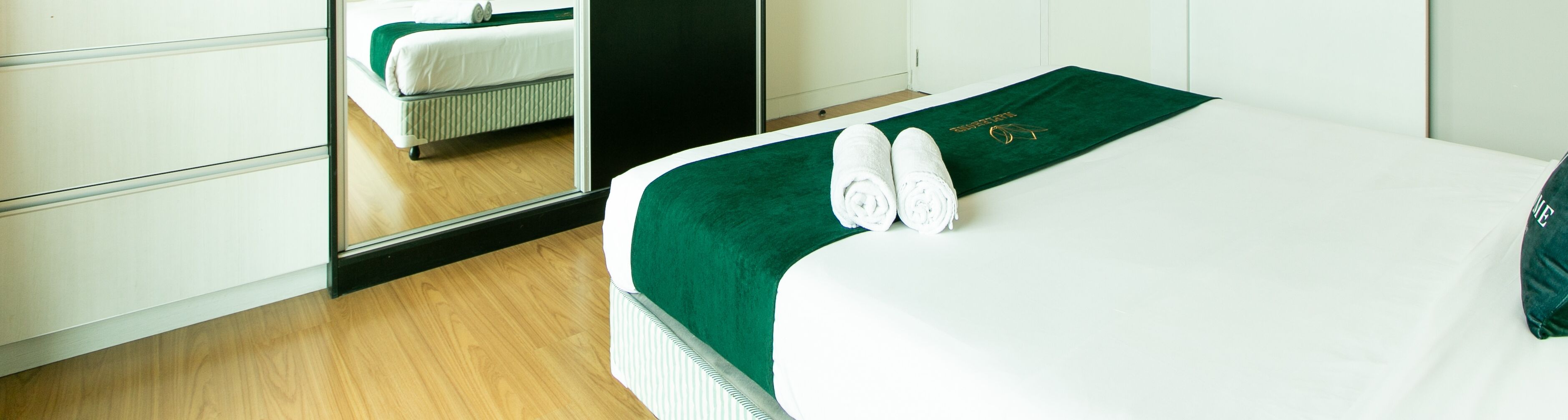 A neatly made bed with a green bedspread and a rolled white towel.