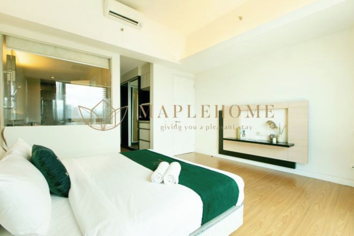 A modern hotel room with a large bed, a green throw blanket, and a small shelf with decorative items.