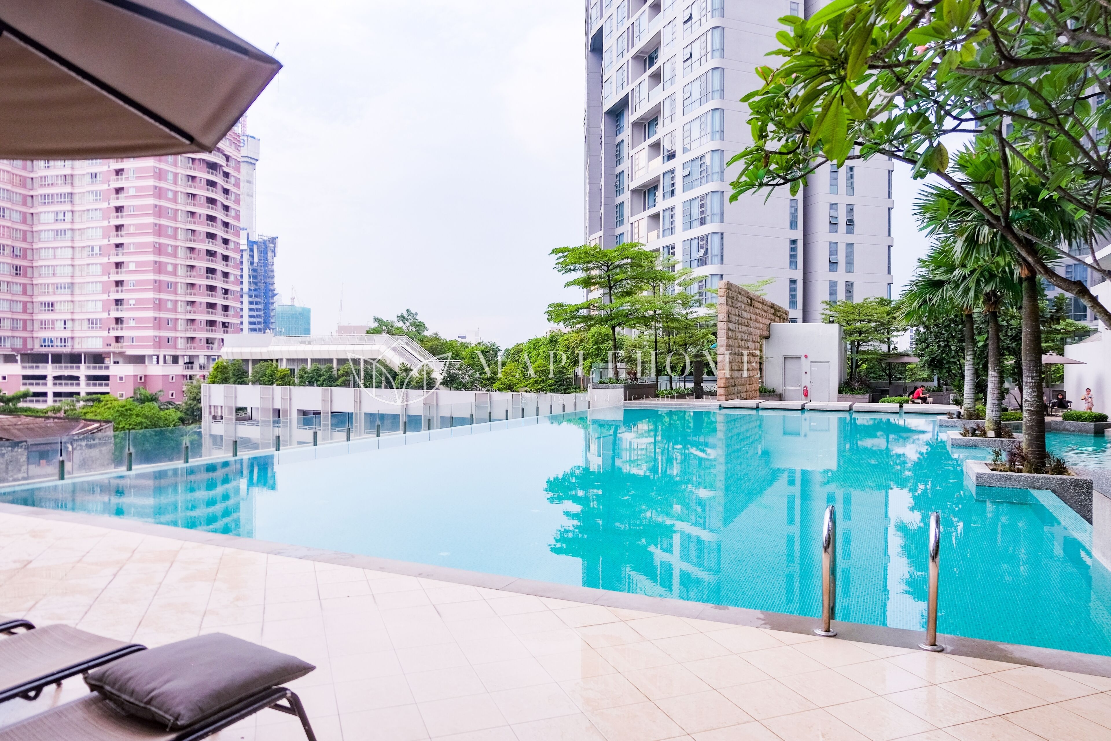 A swimming pool with a tiled deck, surrounded by tall residential buildings and greenery.