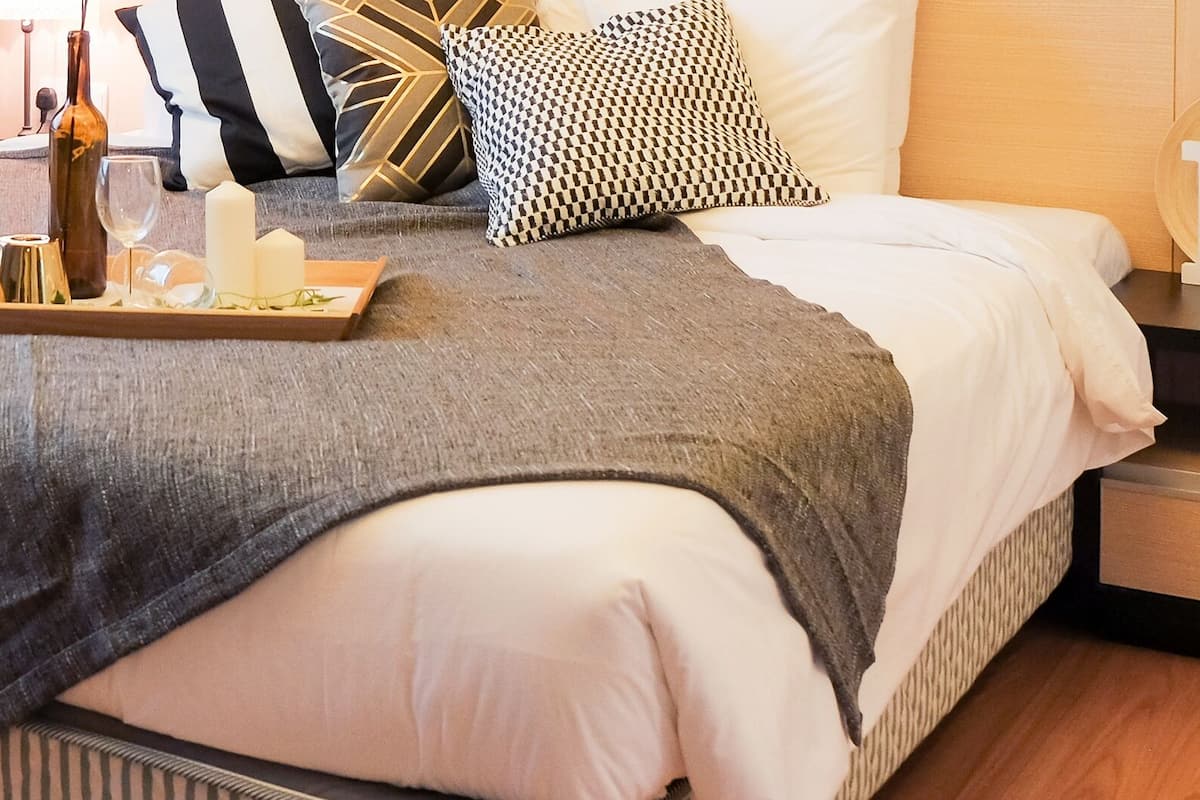 Una cama bien hecha con toallas, una bandeja con velas y una botella de vino.
