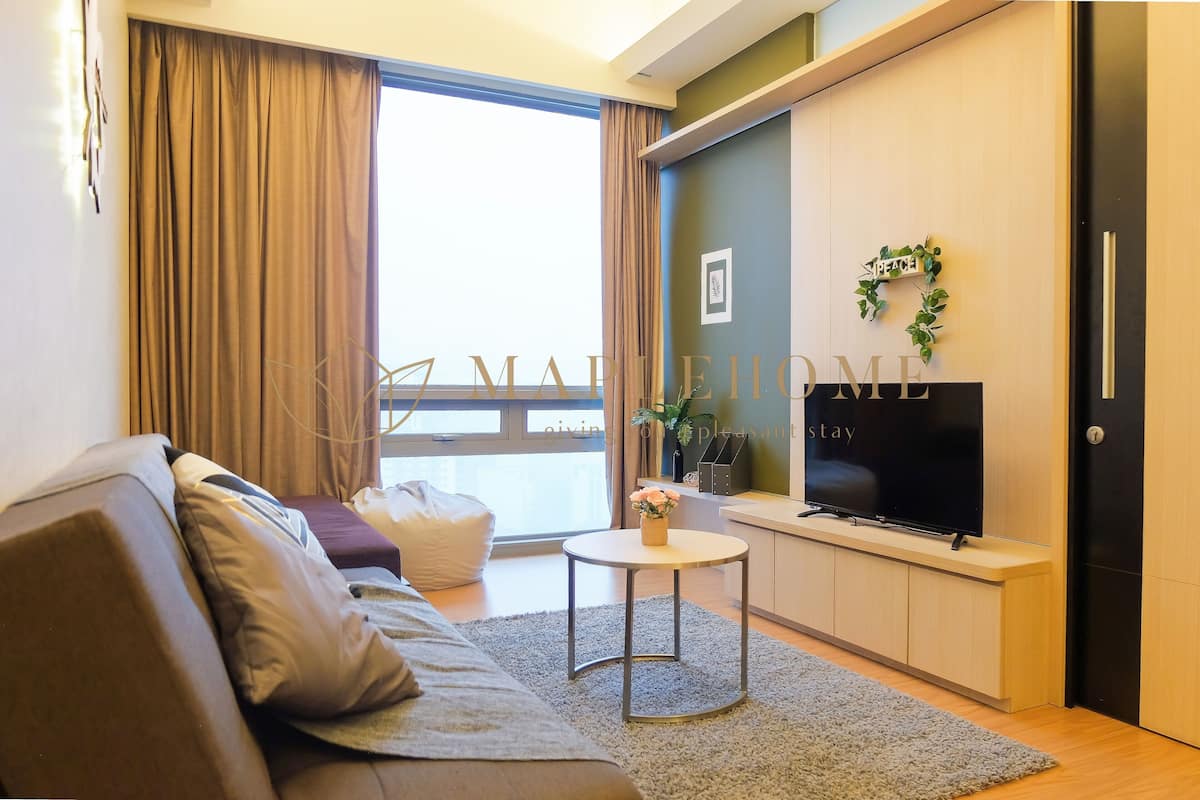 Una sala de estar moderna con un sofá, una mesita, un televisor de pantalla plana y un ventanal con cortinas.