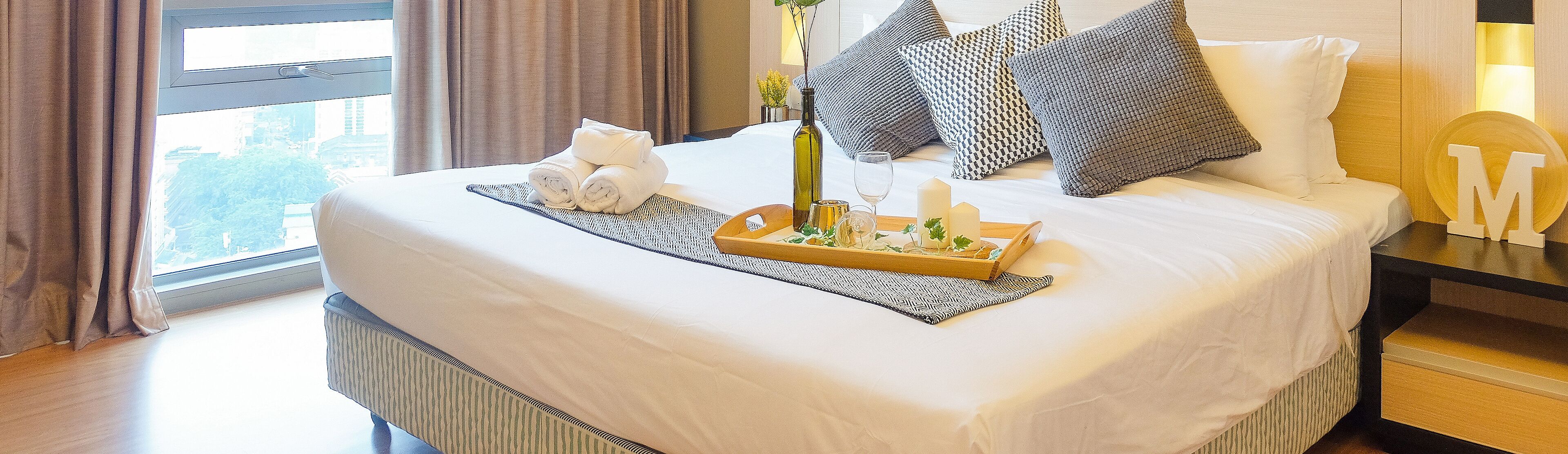 A neatly made bed with a tray of food, a bottle, and a glass.