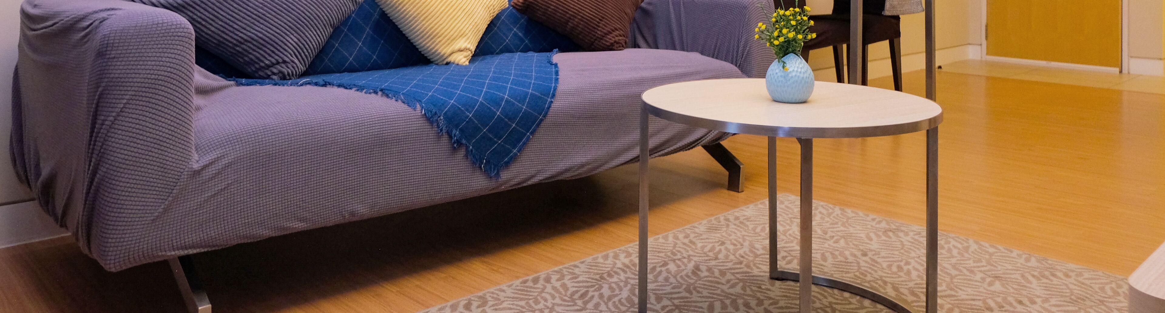 A modern living room with a purple sofa, a small round table, and a vase with yellow flowers.