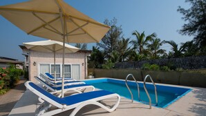 A pool area with lounge chairs and a large umbrella.